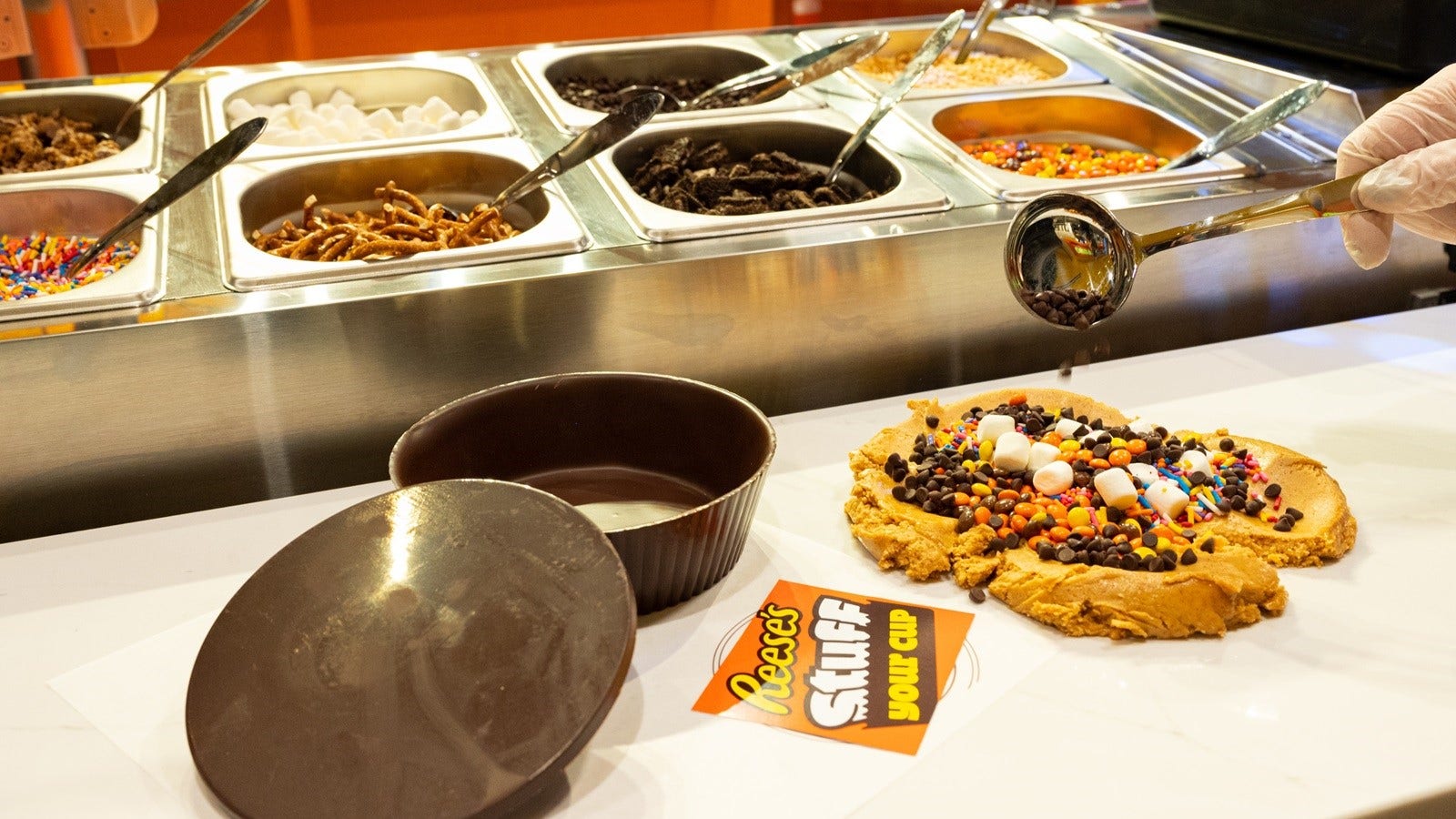 A "Reese's Stuff Your Cup" chocolate station showing in-store experience where advance reservations not required